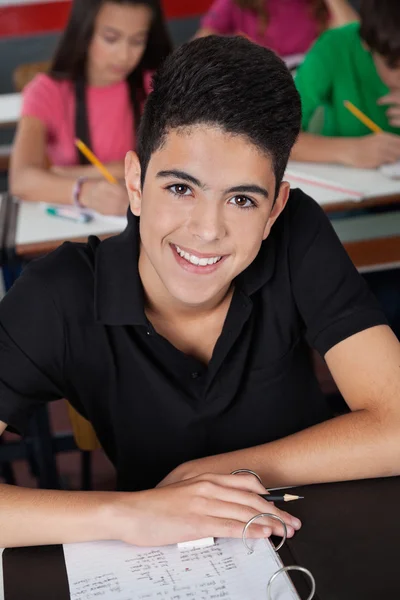 Estudante do ensino médio sorrindo enquanto sentado na mesa — Fotografia de Stock