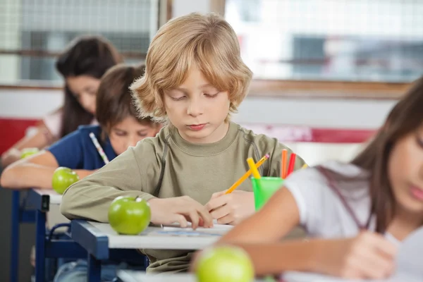 Schoolboy Writing While Sitting At Desk Stock Photo