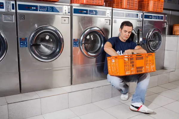 Man With Basket Of Clothes Sitting At Laundromat Stock Photo