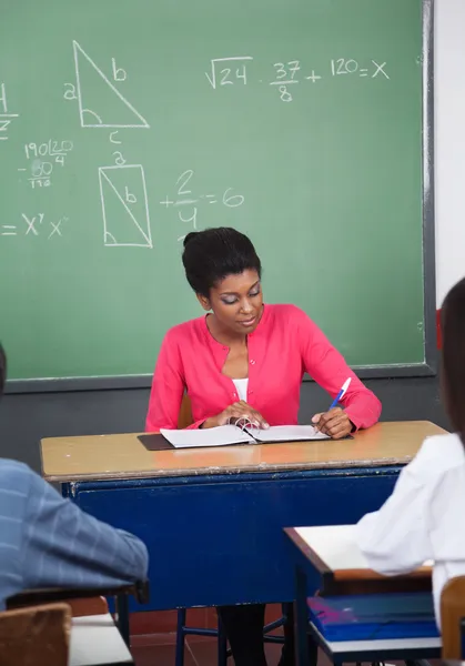 Profesor de escritura en carpeta en el escritorio con los estudiantes en primer plano —  Fotos de Stock