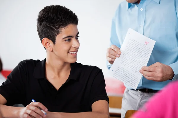 Профессор держит бумагу с мальчиком-подростком за столом — стоковое фото