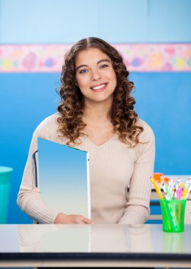 öğretmen masa başında otururken kitap tutan
