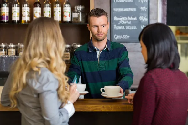 Cantinero sirviendo café a las mujeres en el mostrador en el café —  Fotos de Stock