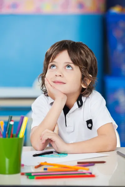 Boy Looking Up While Sitting With Hand On Chin At Desk — Stock Photo, Image