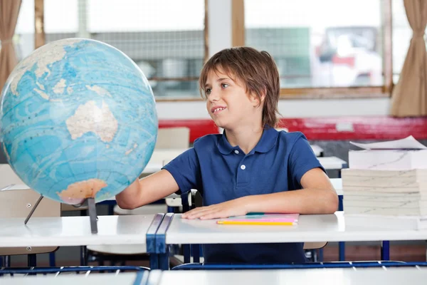 Schoolboy Searching Places On Globe At Desk