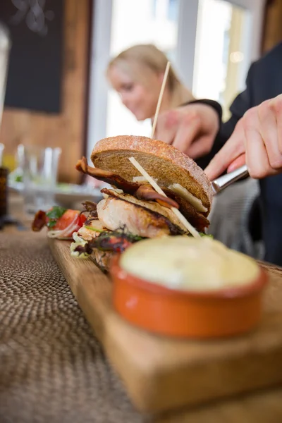 Uomo con hamburger e salsa su piatto di legno — Foto Stock