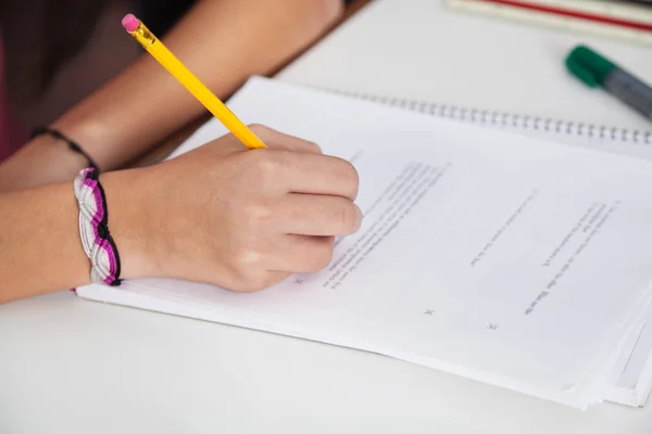 Schoolmeisje schrijven op papier op Bureau — Stockfoto