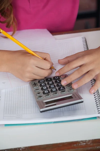 Studentessa adolescente che utilizza la calcolatrice mentre scrive alla scrivania — Foto Stock