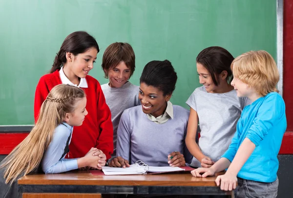 Profesor feliz enseñando a los escolares en el escritorio en el aula — Foto de Stock