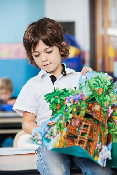 Junge mit Popup-Buch sitzt auf Schreibtisch im Kindergarten — Stockfoto