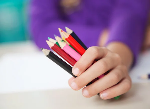 Niña sosteniendo lápices de colores en el escritorio — Foto de Stock