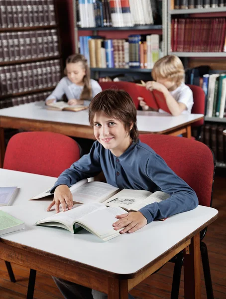 Niño sentado en la mesa con libros con compañeros de clase en segundo plano —  Fotos de Stock