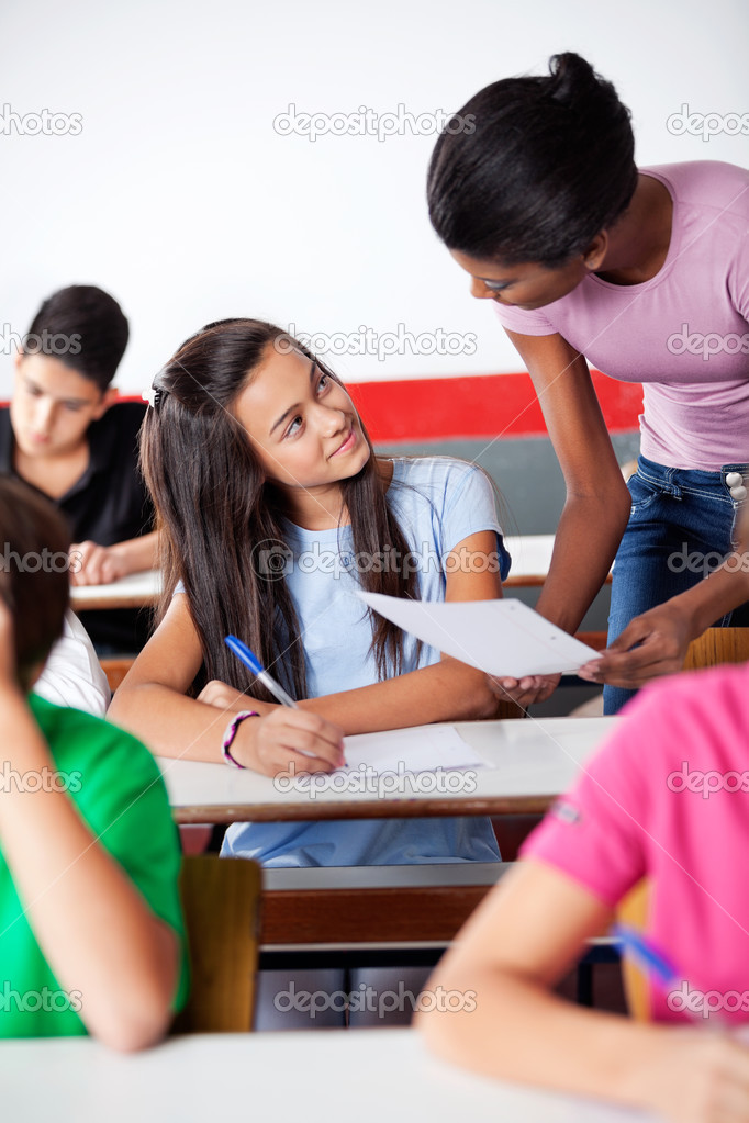 Teacher Assisting Teenage Schoolgirl During Examination In Class