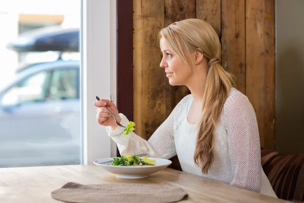 Mulher olhando através da janela enquanto come salada — Fotografia de Stock