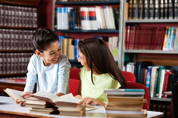 Glad skolflickor tittar på varandra medan de studerar i bibliote — Stockfoto