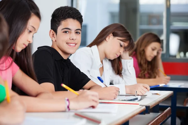 Teenage Boy Sitting With Friends Writing At Desk — Stock Photo, Image