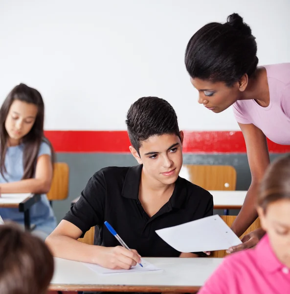 Lehrer zeigt männlichem Schüler am Schreibtisch Papier — Stockfoto