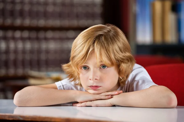 Скучный мальчик смотрит в сторону, когда отдыхает подбородок на руках за столом — стоковое фото