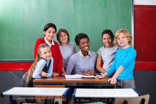 Glad lärare och elever tillsammans på skrivbord i klassrummet — Stockfoto