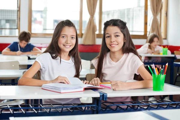 Portrait Of Happy Schoolgirls Sitting With Book At Desk — Stock Photo, Image