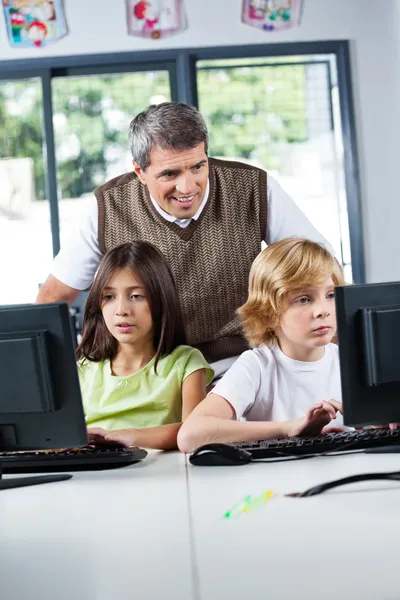 Profesor mirando a los escolares usando PC de escritorio —  Fotos de Stock