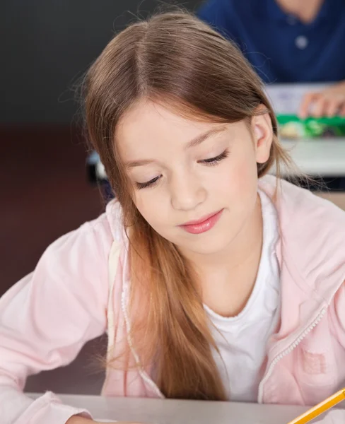 Schoolmeisje schrijven in boek bij klas — Stockfoto