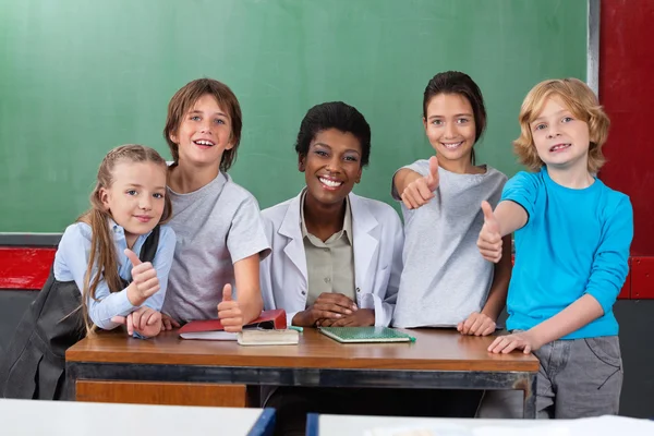 Schüler gestikulieren mit Lehrer am Schreibtisch — Stockfoto