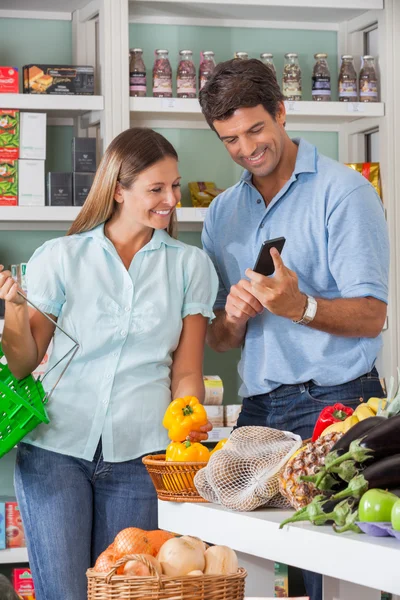 Pareja usando móvil mientras compras en supermercado —  Fotos de Stock