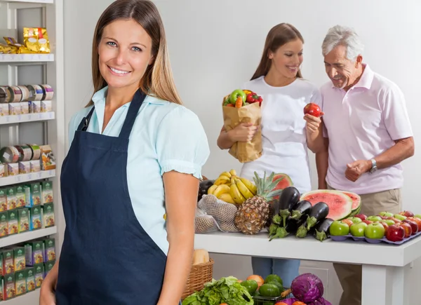 Butiksbiträde med familj shopping i bakgrunden — Stockfoto