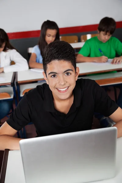 Adolescente feliz Schoolboy sentado com laptop na sala de aula — Fotografia de Stock