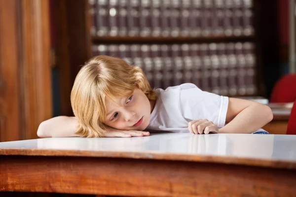 Doordachte schooljongen leunend op tabel in bibliotheek — Stockfoto