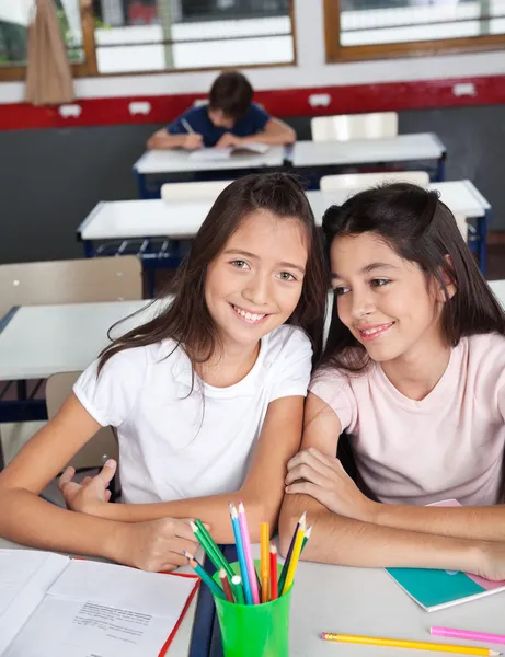 Schoolmeisje zitten met klasgenoot aan balie in klas — Stockfoto