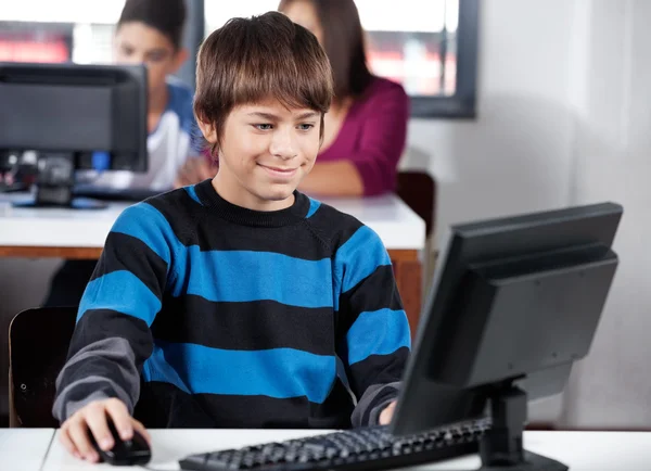 Pojke leende medan du använder datorn i klassrummet — Stockfoto