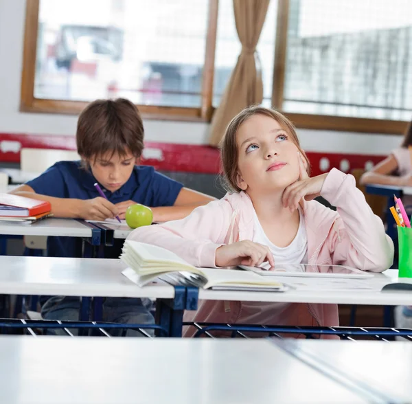 Écolière réfléchie levant les yeux tout en utilisant la tablette dans la salle de classe — Photo