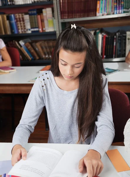 Studentin liest Buch am Tisch in Bibliothek — Stockfoto