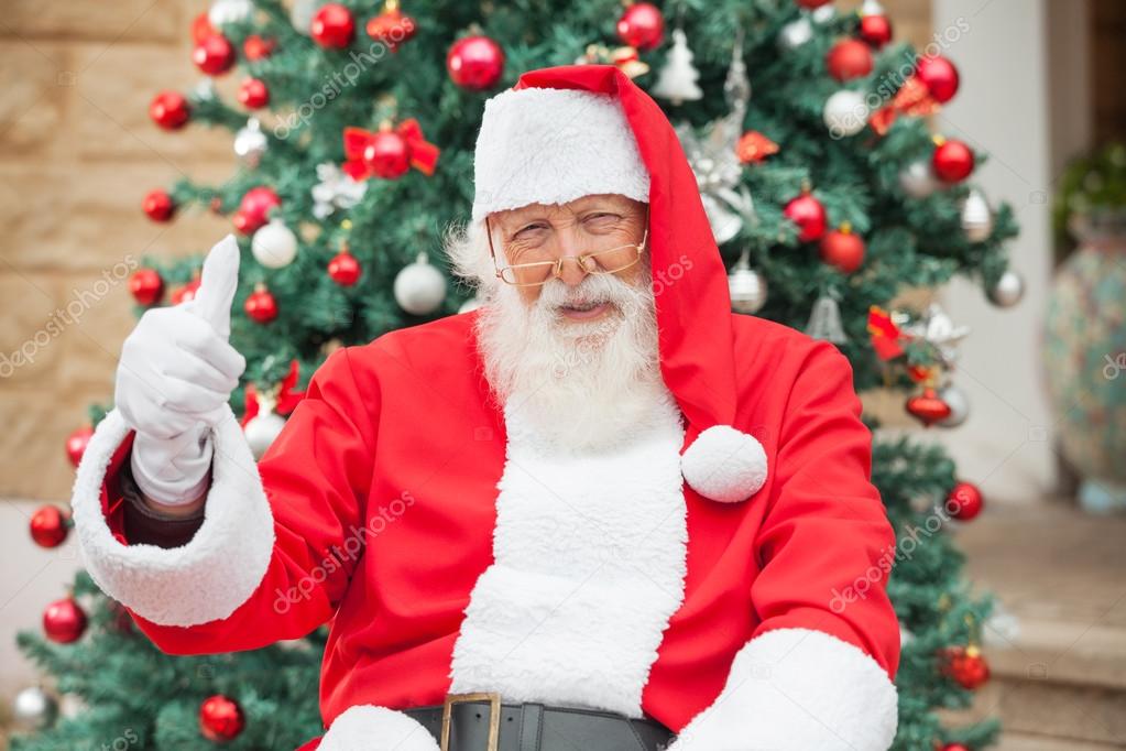 Santa Claus Gesturing Thumbsup Against Christmas Tree