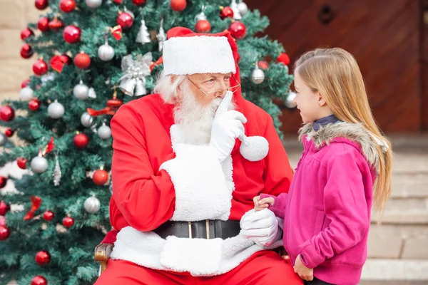 Menina olhando para Papai Noel Gesturing dedo nos lábios — Fotografia de Stock