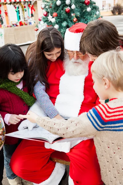 Papá Noel con niños señalando el libro —  Fotos de Stock