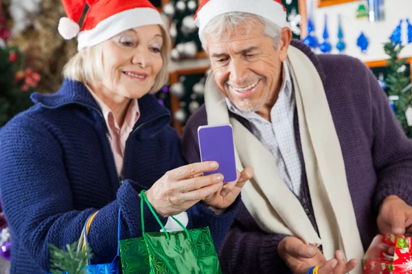 Pareja mayor usando el móvil en la tienda de Navidad —  Fotos de Stock
