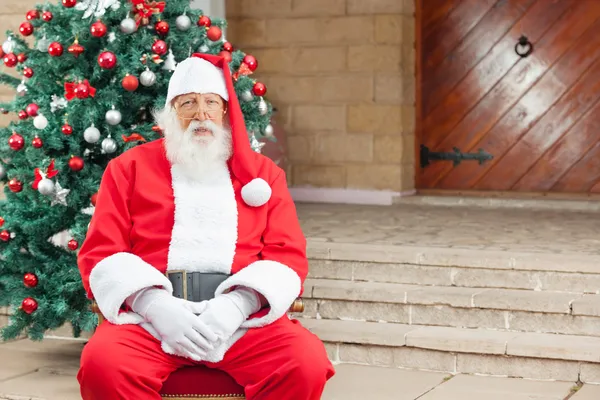 Santa claus sedí proti vánoční strom — Stock fotografie