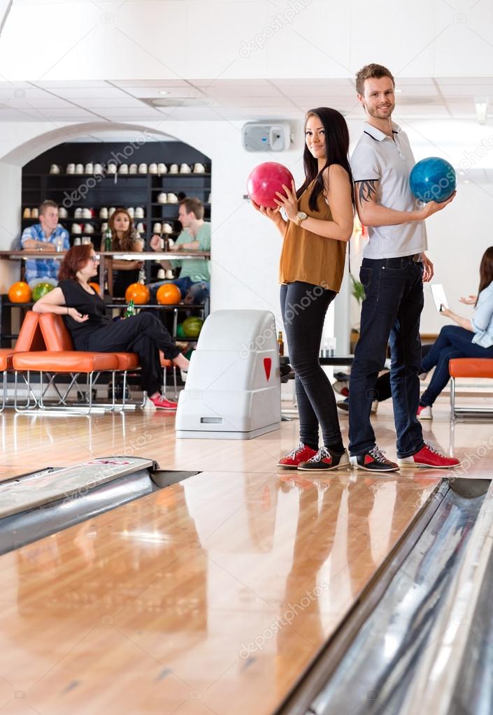Man And Woman Standing With Bowling Balls in Club
