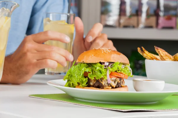 Hamburguesa con la mano del hombre sosteniendo la bebida en la mesa — Foto de Stock