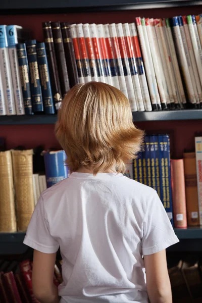 Школьник, стоящий против книжной полки в библиотеке — стоковое фото