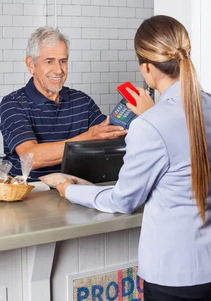 Kvinnliga kunden betalar via mobiltelefon i butik — Stockfoto