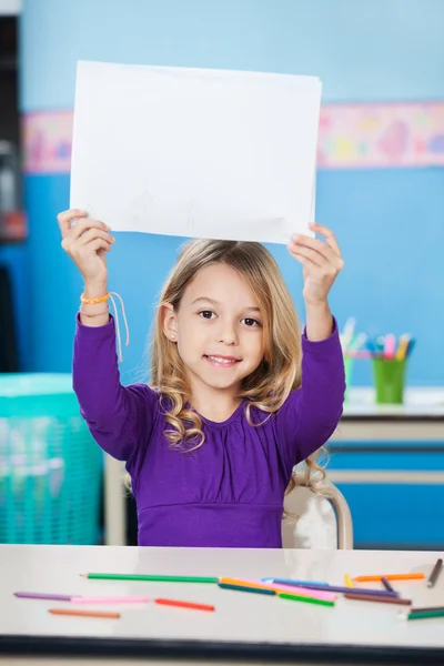 Niña sosteniendo papel en blanco en el escritorio en el aula —  Fotos de Stock