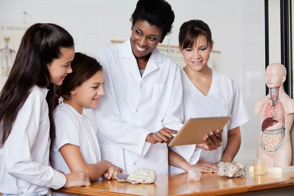 Insegnante guardando studentesse durante l'utilizzo di tablet in biologia Cla — Foto Stock