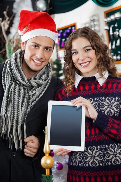 Pareja feliz mostrando la tableta digital en la tienda de Navidad —  Fotos de Stock