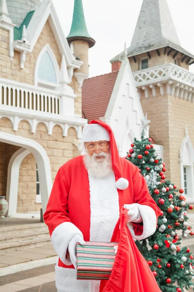 Weihnachtsmann steckt Geschenk in Tüte vor Haus — Stockfoto