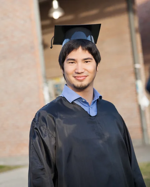 Estudiante masculino vestido de graduación y tablero de mortero en el campus — Foto de Stock