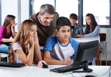 erkek öğretmen bilgisayar dersinde öğrencilere yardım